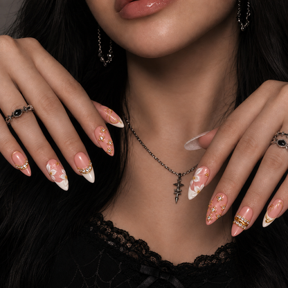 Model mockup showing blush-pink nails with white florals, gem borders, and gold-tone swirls on hands posed near the neckline.