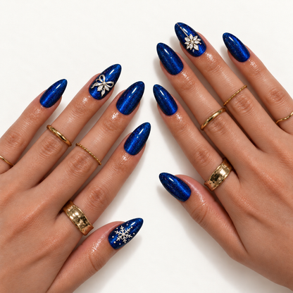 Hand-model mockup showing pointed blue shimmer nails with snowflake, ribbon-bow, and jewel-like floral accents, styled with gold-toned rings.