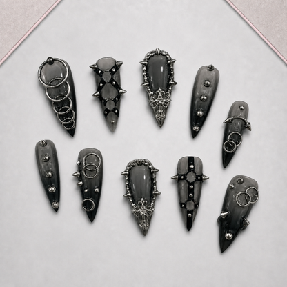 Iron Reliquary press-on nail set displayed on an approved tray, showing varied dark gothic ring, stud, and spike motifs.