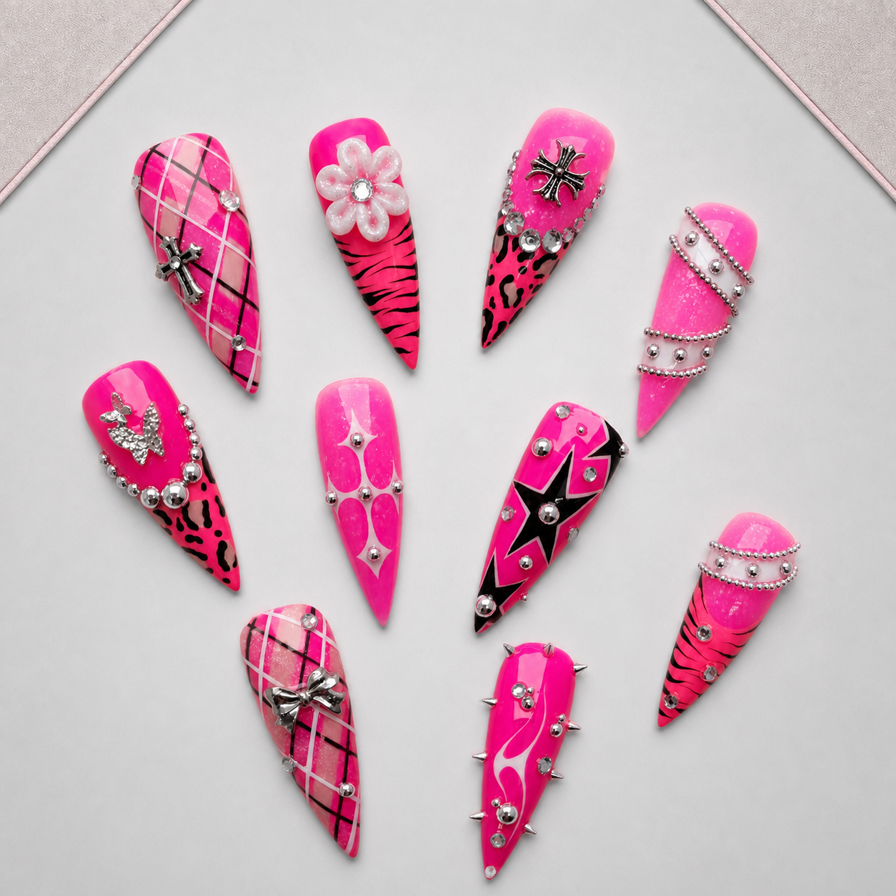 Pink Rebel Mix press-on nails arranged on an approved display tray, showing varied graphic art and silver-toned embellishments.