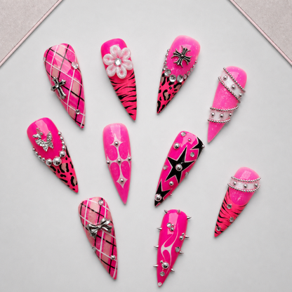 Pink Rebel Mix press-on nails arranged on an approved display tray, showing varied graphic art and silver-toned embellishments.
