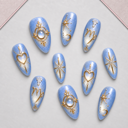 Light-blue celestial-inspired press-on nail set displayed on an approved tray, with gold linework and crystal-like accents.