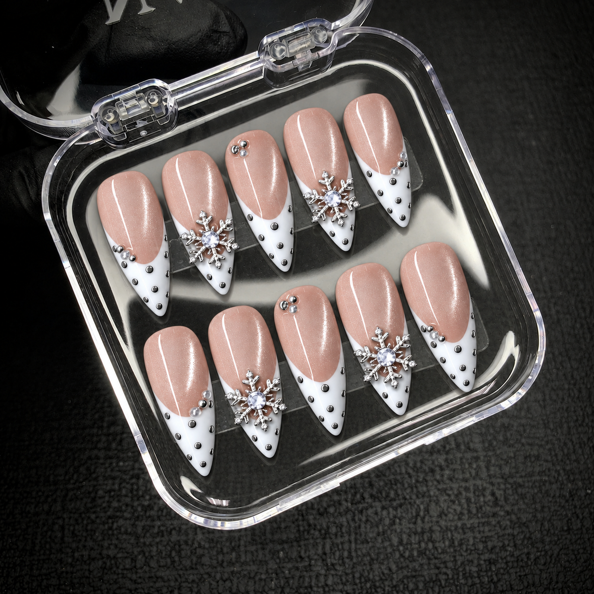 Open clear display box holding ten Pearl Snowfall nails against a dark background, with white pointed tips and silver snowflake accents visible.