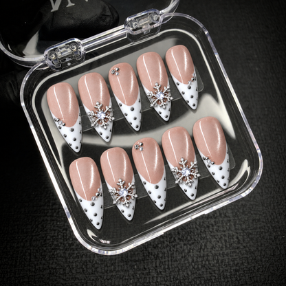 Open clear display box holding ten Pearl Snowfall nails against a dark background, with white pointed tips and silver snowflake accents visible.
