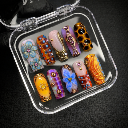 Open clear case holding ten coordinated floral and abstract decorated nails on a dark textured surface.