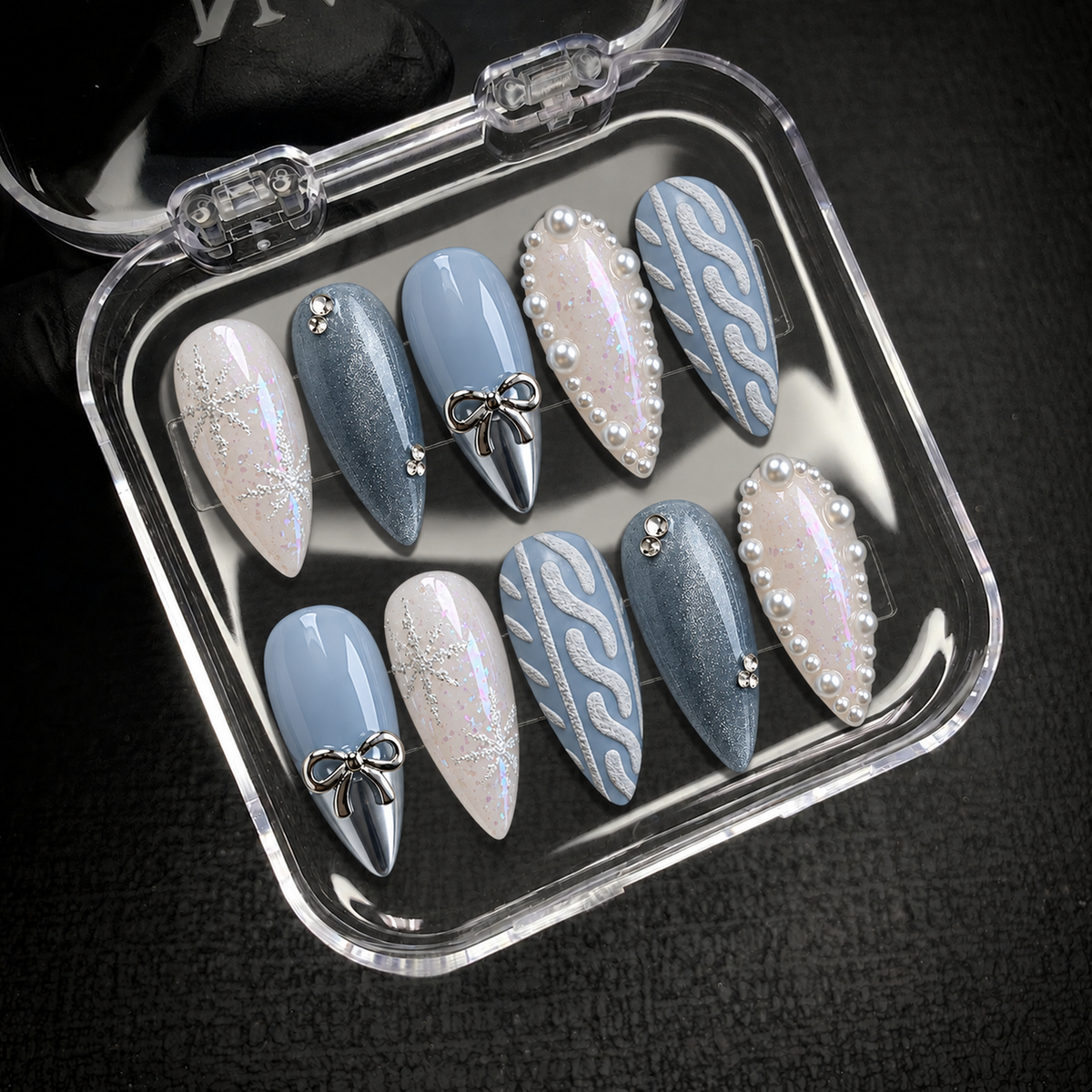 Open clear case displaying ten coordinated Frosted Blue Bow nails against a dark background.