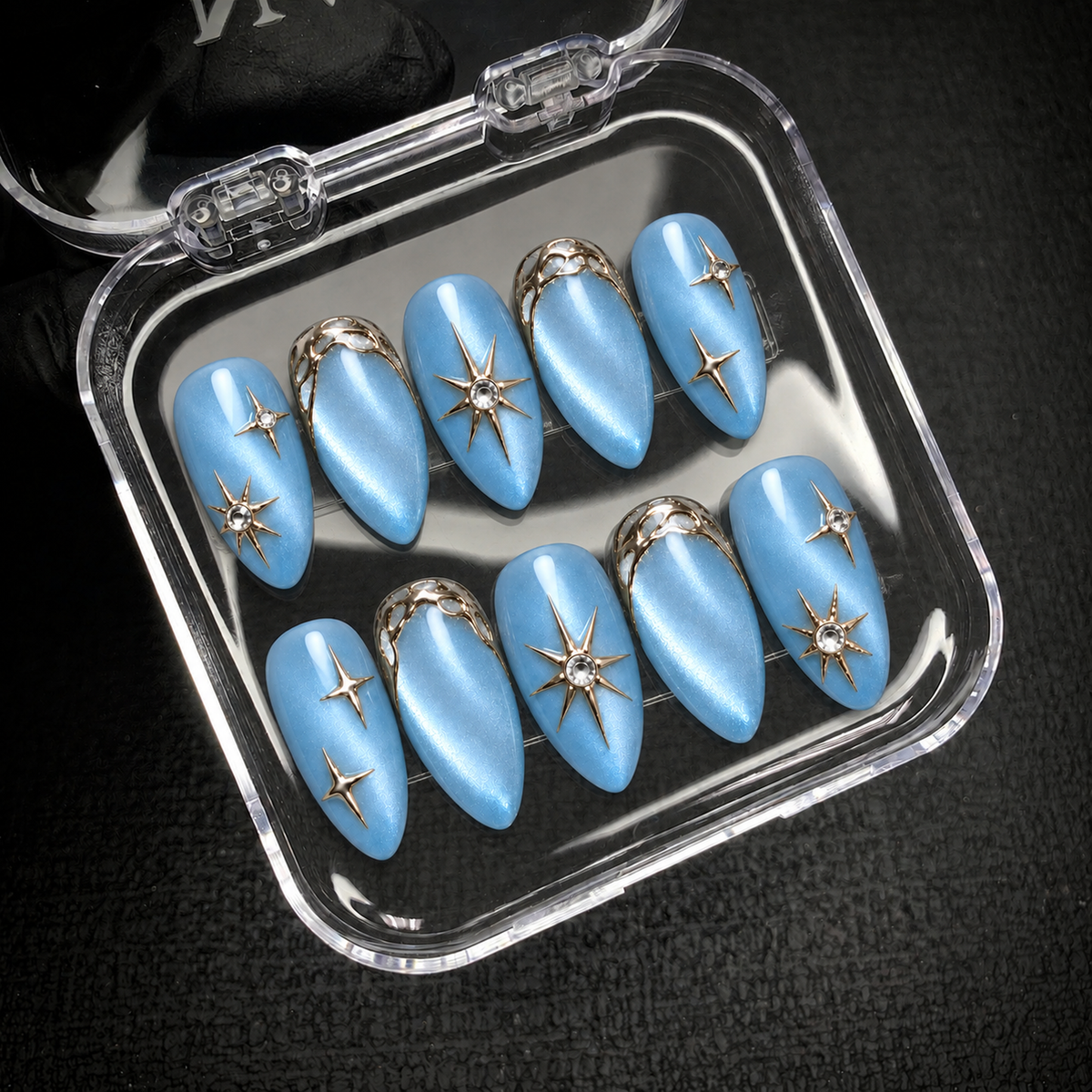 Ten blue starburst nails arranged inside an open clear case against a dark background.