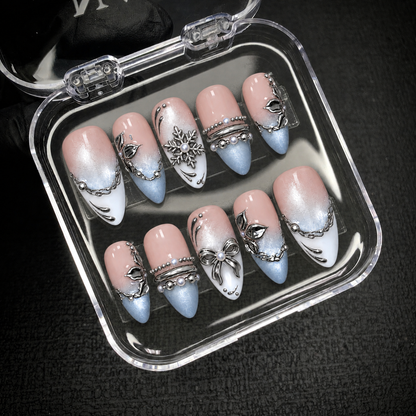 Ten blush pink, icy blue, and white nails with silver-tone details displayed inside an open clear case against a dark background.