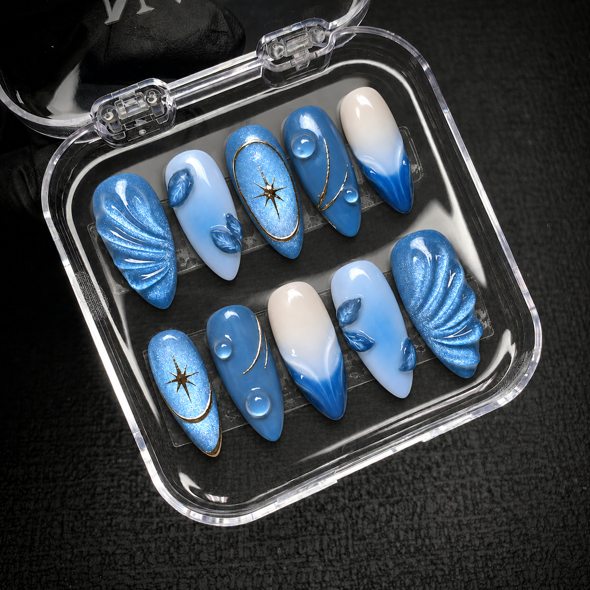 Open clear case displaying ten Celestial Blue Tide nails in two rows against a dark background.