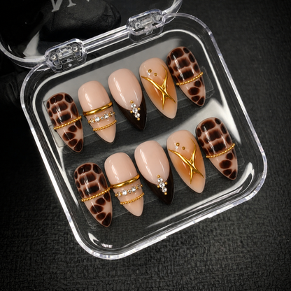 Open clear case holding ten coordinated nude and brown embellished nails in two rows on a dark textured background.
