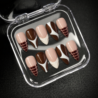 Open clear nail case on dark textured fabric holding ten coordinated nude pink and cocoa brown nails with ivory curves and croc-inspired tips.