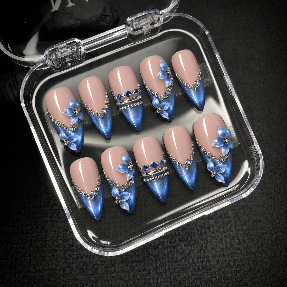 Ten blush pink and shimmering blue nails displayed in an open clear case against a dark background.