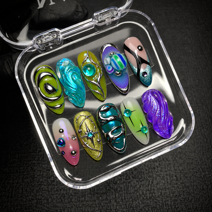 Open clear nail case on a dark textured surface holding ten coordinated nails with colorful waves, silver-colored outlines, and orbital details.