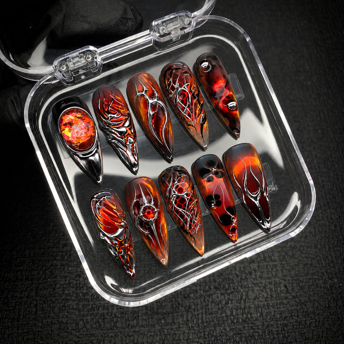 Open clear case holding ten Molten Chrome nails with fiery red-orange accents and silver linework on a dark textured background.