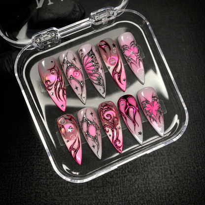 Open clear case holding ten coordinated pink, gray, silver, and magenta nails in two rows on a dark textured surface.