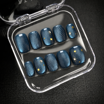 Ten navy-blue nails with curved textures and gold star accents displayed inside an open clear case.