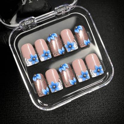 Ten Frosted Blue Petals nails displayed inside an open clear case against a dark background, showing blue flowers and rose-toned accent nails.