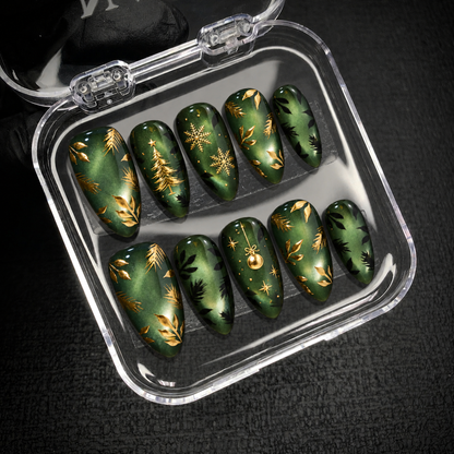 Open clear case holding ten green and gold Christmas nails in two rows on dark textured fabric.