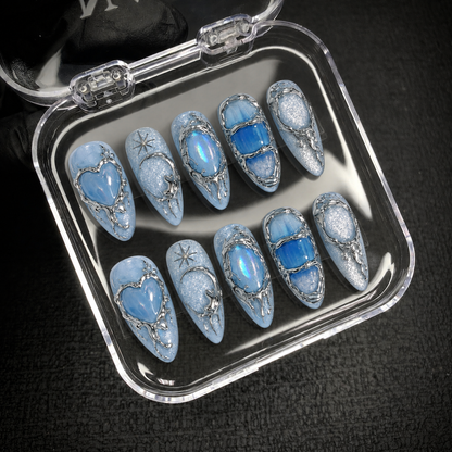 Open clear case displaying ten coordinated icy blue nails with heart, crescent, oval, and blue panel designs.