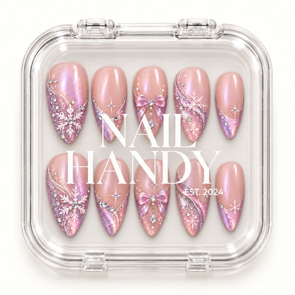 Closed clear Nail Handy case displaying ten blush pink nails with snowflakes, bows, lavender shimmer, and gem accents beneath white lid lettering.