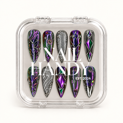 Closed clear Nail Handy case displaying ten dark prismatic nails with silver-toned ornament, purple and green diamond motifs, and silver-gray accents.