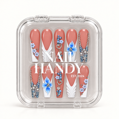 Closed clear Nail Handy case displaying ten coral-pink nails with blue flowers, white sculpted accents, heart ornaments, and clear and blue rhinestone details.