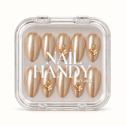 Closed clear Nail Handy case displaying ten champagne shimmer nails with gold-tone holly leaves and ivory pearl-like accents beneath white lid lettering.