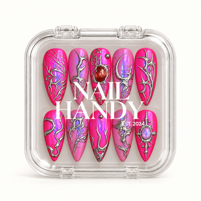 Closed clear Nail Handy case displaying ten pink nails with iridescent shimmer, silver-toned ornamentation, and red and lavender jewel-like accents.