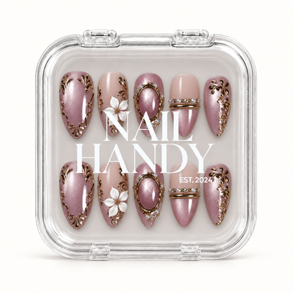Closed clear Nail Handy case displays ten coordinated mauve and blush nude nails beneath white branding, with floral and gold-toned ornamental details.