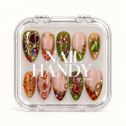 Closed clear Nail Handy case displaying ten olive, blush, and amber nails with ornate gold-tone details beneath white lid lettering.