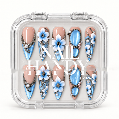 Clear presentation box holding ten blush pink and blue floral press-on nails, with Nail Handy lettering across the front.