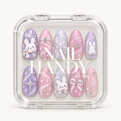 Closed clear case with white Nail Handy lettering displaying ten pink and lavender nails decorated with bunnies, snowflakes, bows, and shimmering accents.