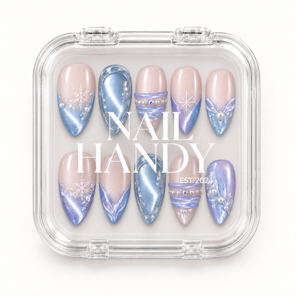 Closed clear case with white Nail Handy lettering displays ten winter nails with icy blue shimmer, lilac accents, snowflakes, and pearl-like details.