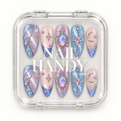 Closed clear presentation box with white lettering, showing ten blue, lilac, and blush pink nails decorated with celestial and snowflake motifs.