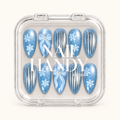 Closed clear case displaying ten icy blue snowflake, bow, and silver-striped nails beneath white lettering on the lid.