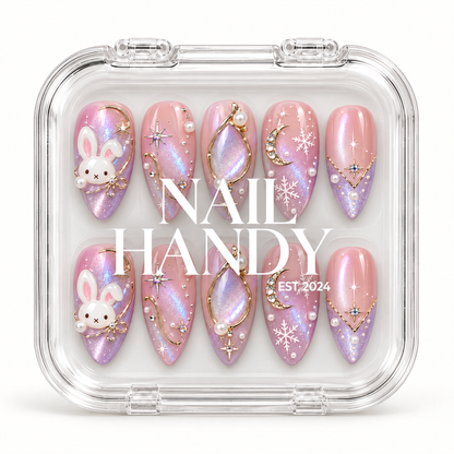 Closed clear case with white Nail Handy lettering, displaying ten pink and lilac shimmer nails with bunny accents and winter celestial details.