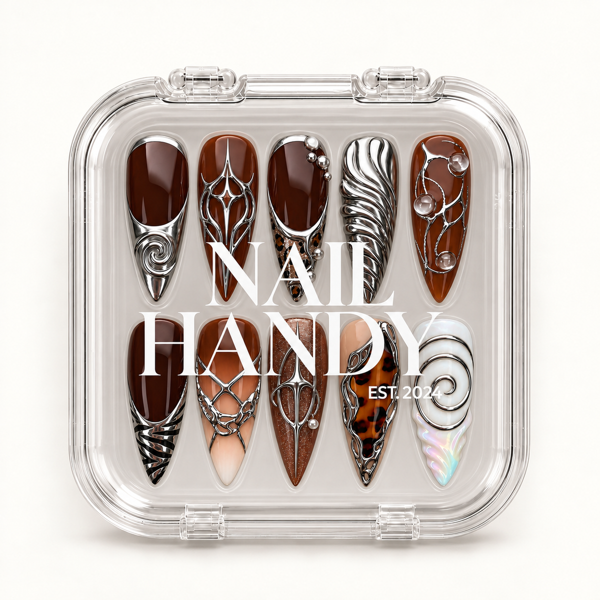 Closed clear case displaying ten coordinated nails with brown bases, silver-toned sculptural accents, and a white spiral design beneath Nail Handy lettering.