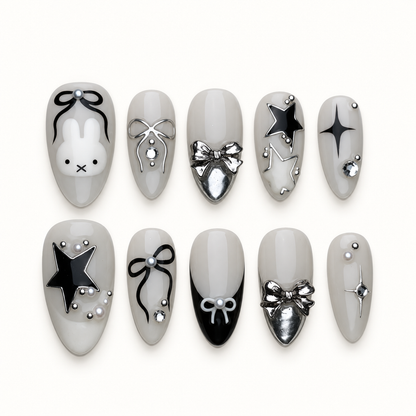 Ten glossy greige press-on nails arranged in two rows, featuring a bunny face, bows, stars, silver accents, and a black tip.