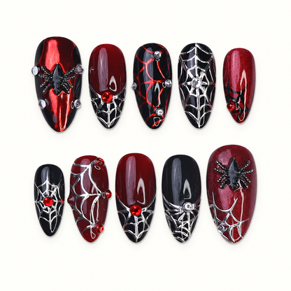 Ten coordinated crimson red and black press-on nails with silver spiderweb linework, raised spider accents, and red gem-like details on a light neutral background.