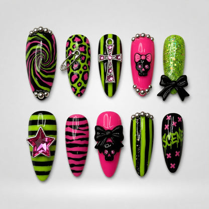 Ten coordinated hot pink, black, and lime green press-on nails arranged in two rows, with stripes, swirls, bows, skull motifs, glitter, and jeweled-style accents.