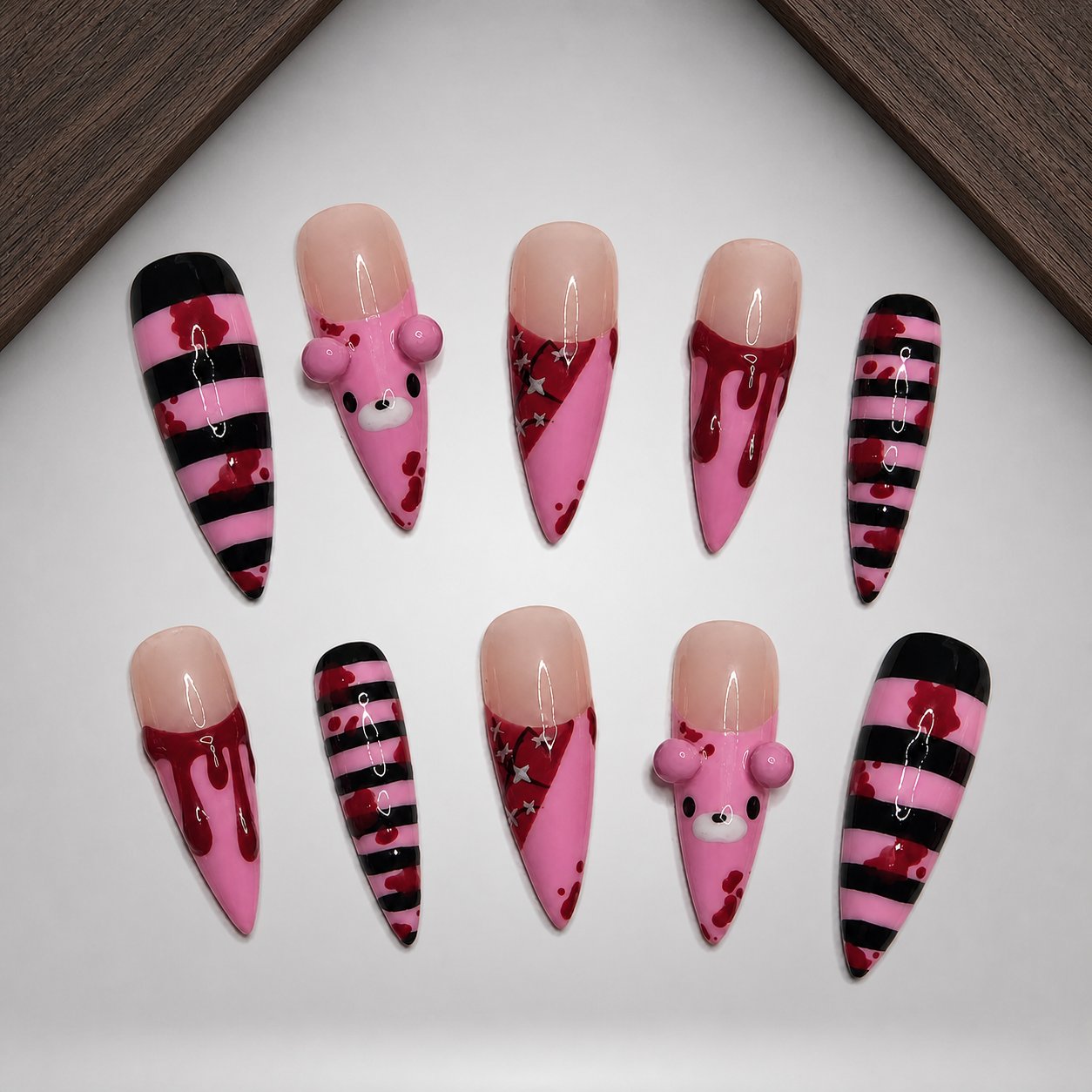 Cherry Stripe Mischief nail set arranged on a walnut tray, showing striped and heart-detailed pink designs.